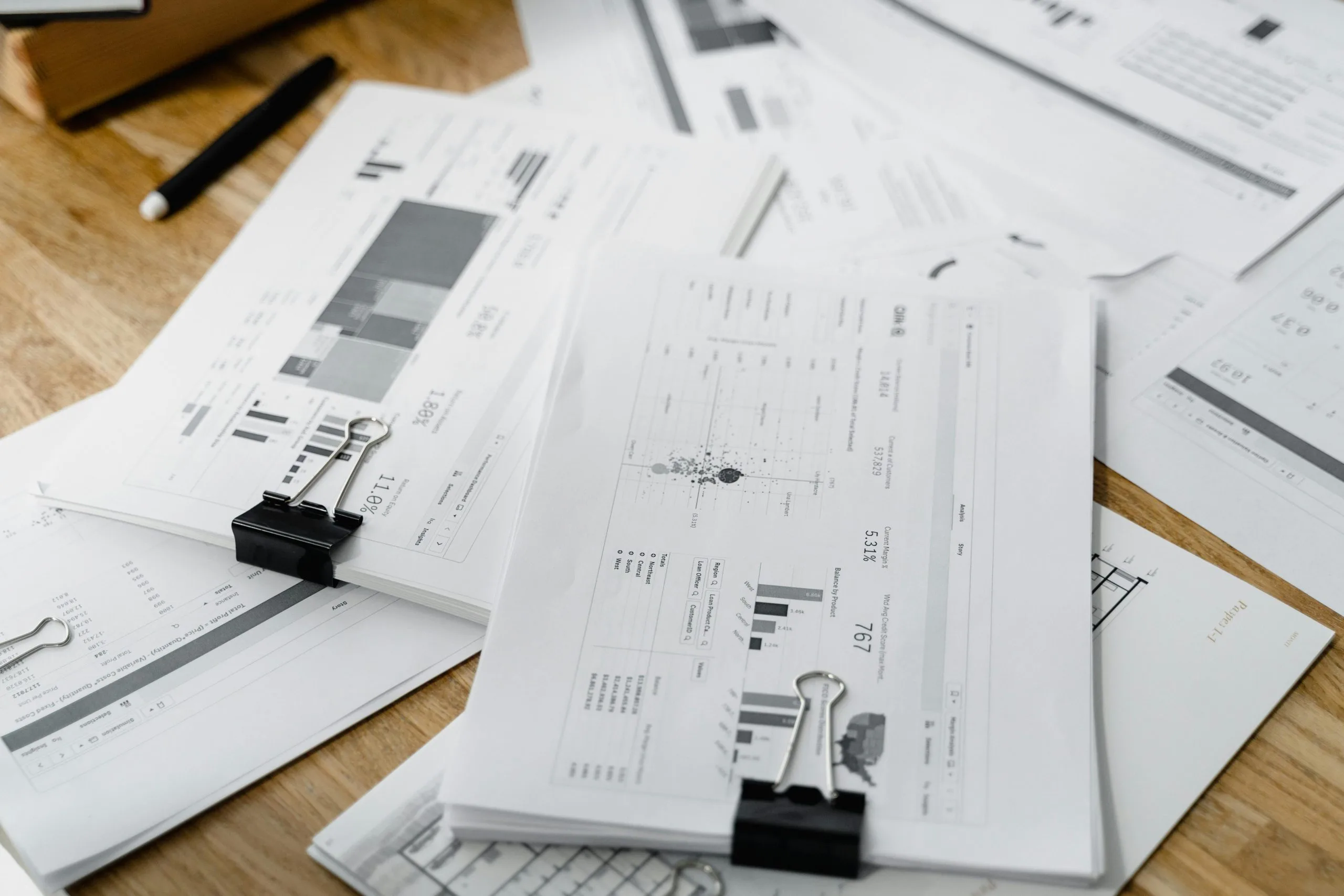 Home A stack of financial reports and graphs with clips on a wooden desk, highlighting business planning.