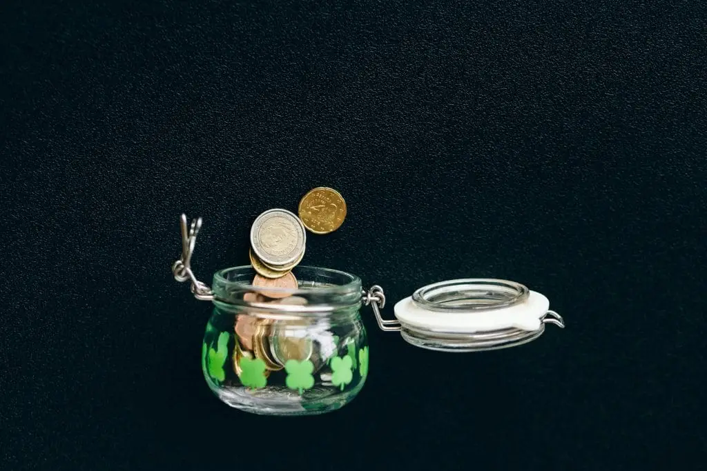 How To File a VAT Return in the UK – Step-By-Step Guide for Small Businesses Glass jar with coins falling into it on a black background, symbolizing savings.
