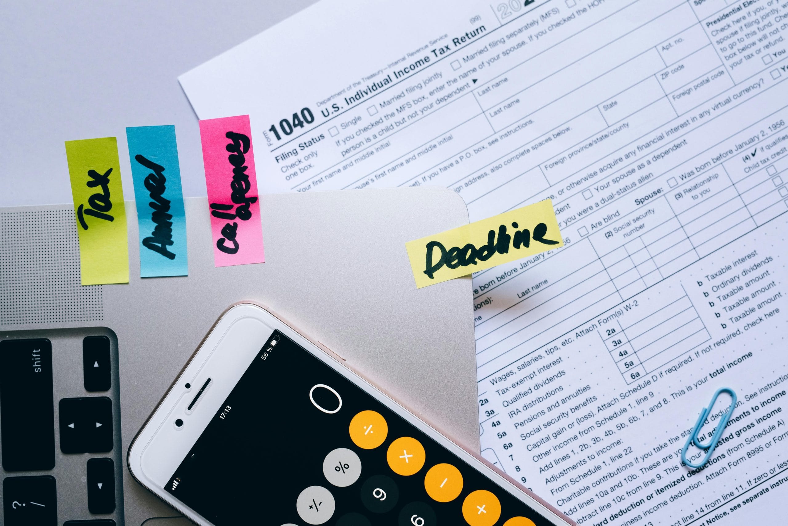 Services Office desk flat lay showing tax documents, calculator app on smartphone, sticky notes, and paperclips.
